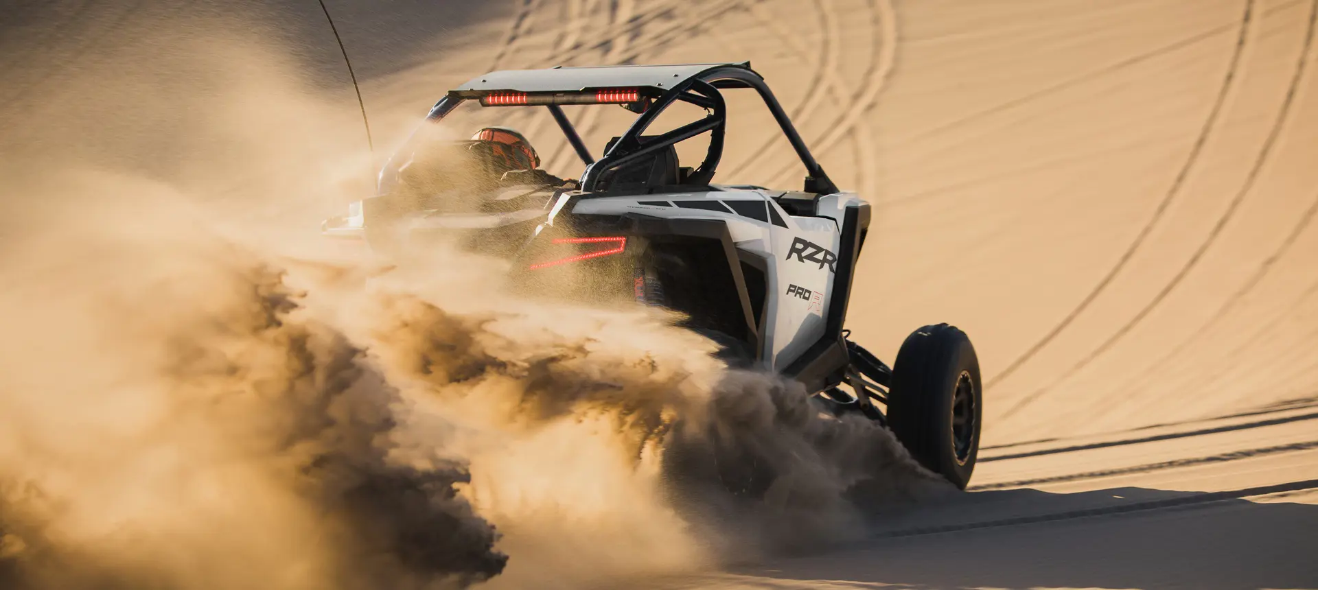 A whtie crystal Polaris RZR Pro R side-by-side throwing sand in the desert.