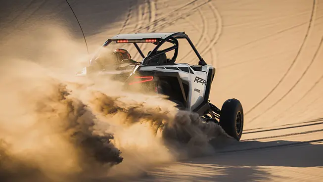 A whtie crystal Polaris RZR Pro R side-by-side throwing sand in the desert.