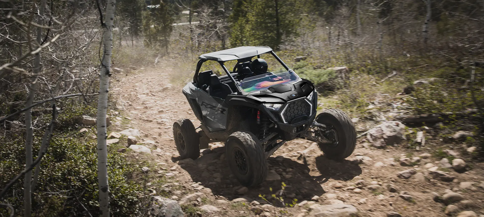 Polaris RZR Pro S side-by-side climbing over rocky terrain on a forest trail.