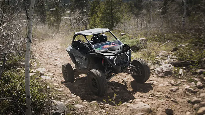 Polaris RZR Pro S side-by-side climbing over rocky terrain on a forest trail.