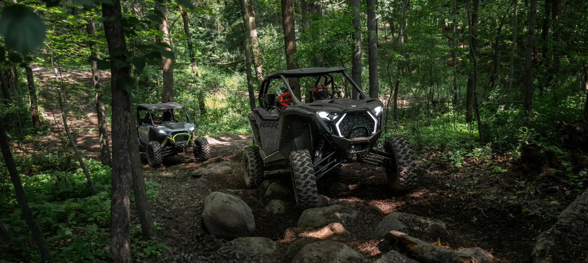 2 Polaris RZR Pro XP side-by-sides trail riding over rocky terrain.