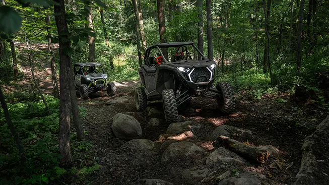 2 Polaris RZR Pro XP side-by-sides trail riding over rocky terrain.