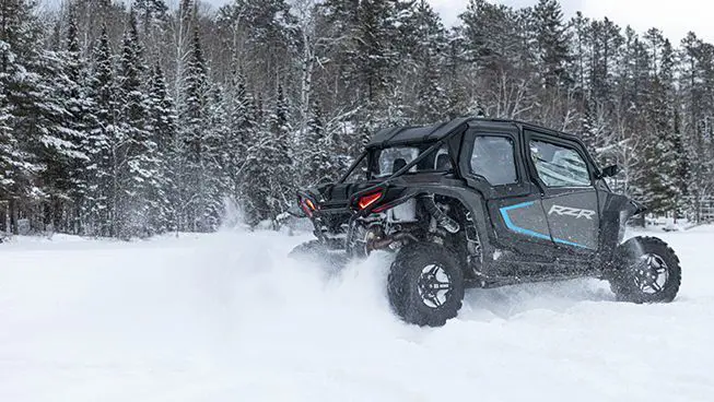 Side profile of a RZR XP side-by-side driving in the winter.