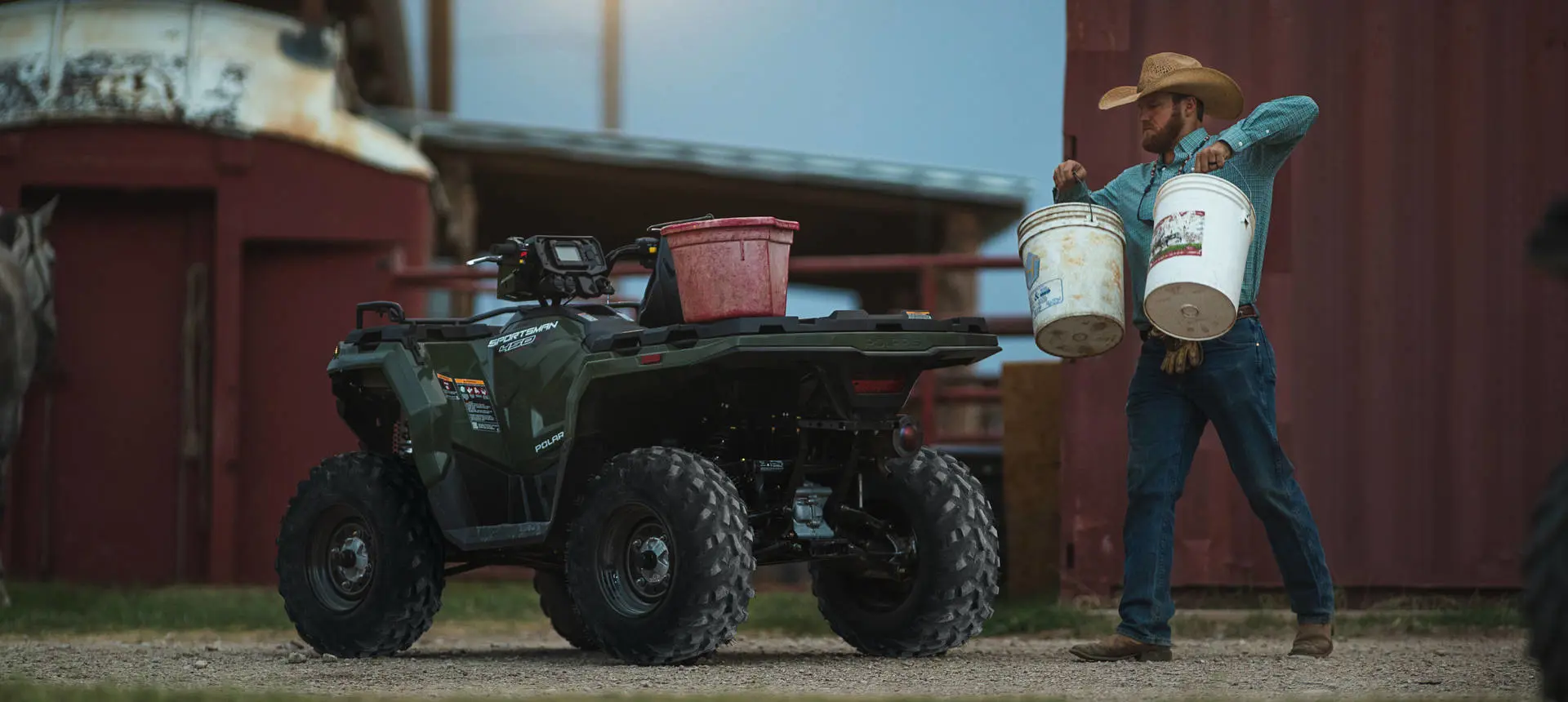 A farmer carrying buckets toward a Polaris Sportsman 450 H.O. ATV.