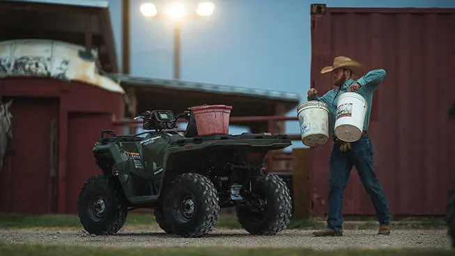 A farmer carrying buckets toward a Polaris Sportsman 450 H.O. ATV.