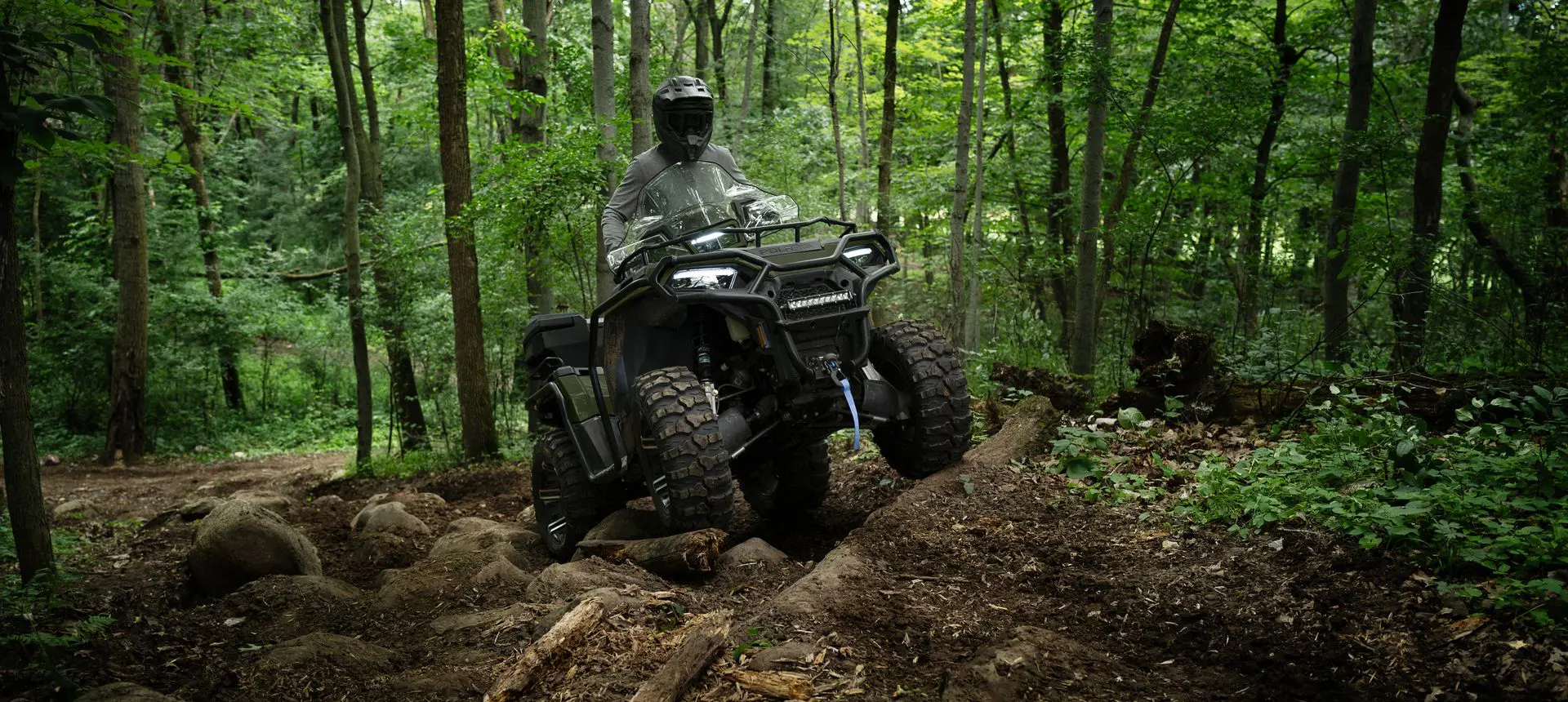 Rider on a Polaris Sportsman 570 ATV driving over uneven terrain in the forest.