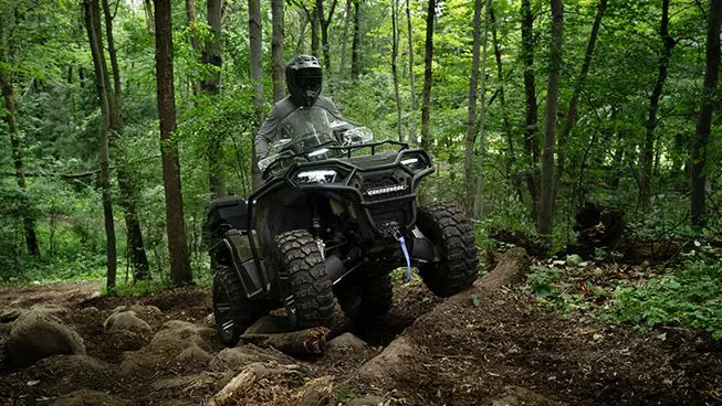 Rider on a Polaris Sportsman 570 ATV driving over uneven terrain in the forest.
