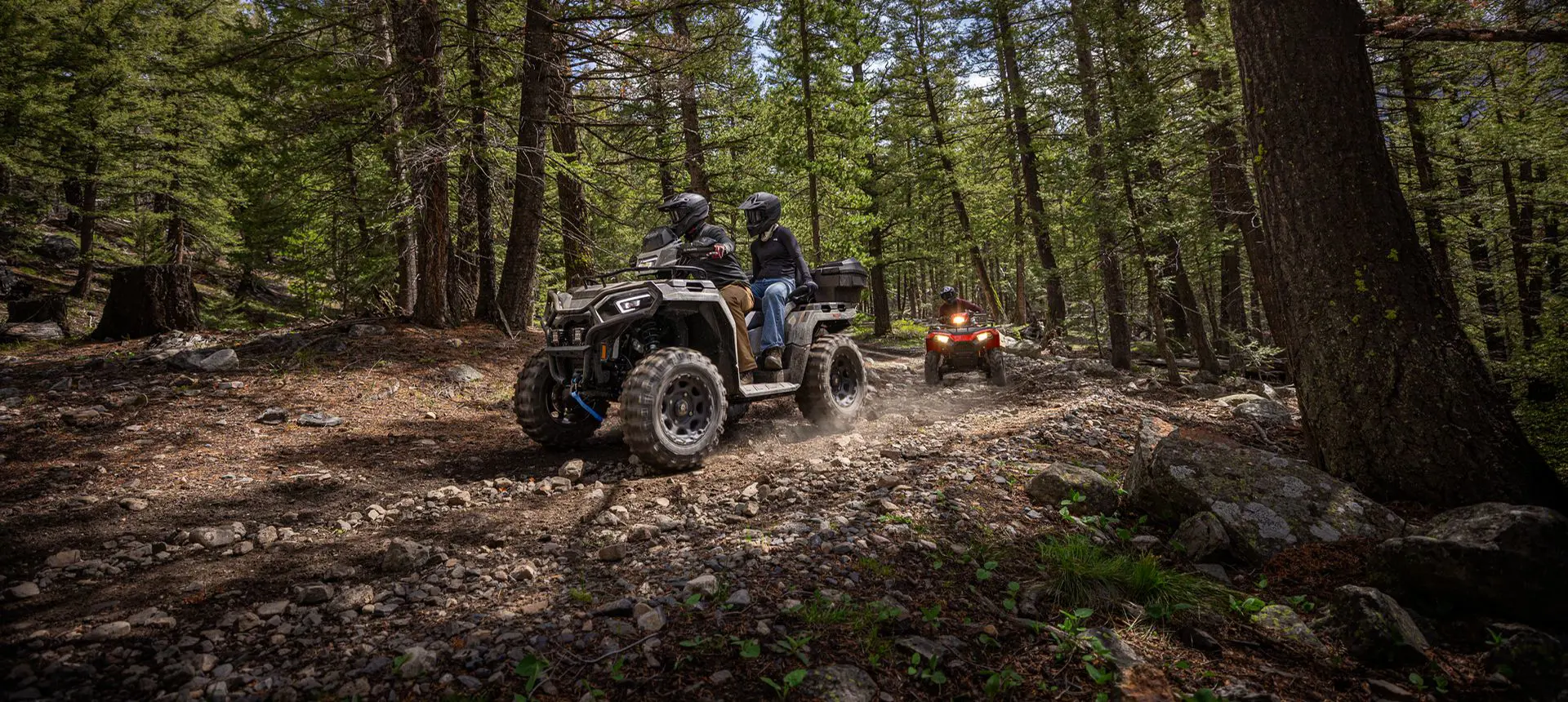 2 riders on a Polaris Sportsman Touring 570 ATV driving on a forest trail.