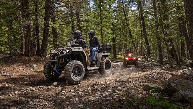 2 riders on a Polaris Sportsman Touring 570 ATV driving on a forest trail.