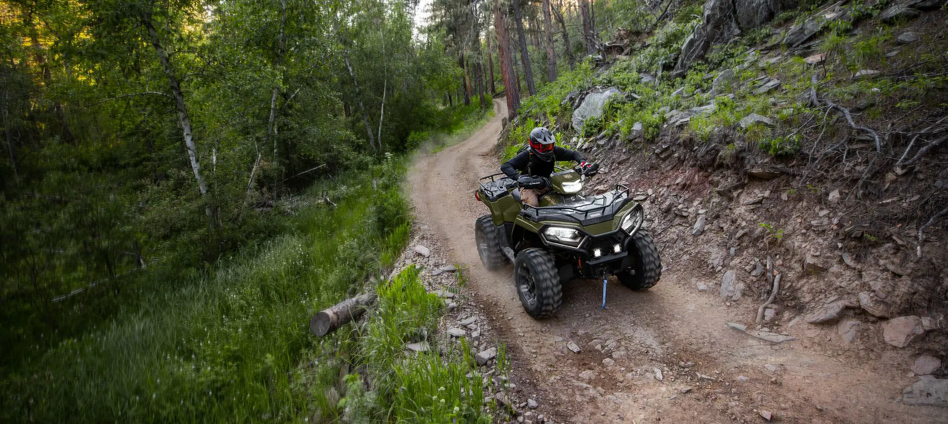 A rider on a Polaris Sportsman 570 ATV driving on a well-ridden trail in the forest.