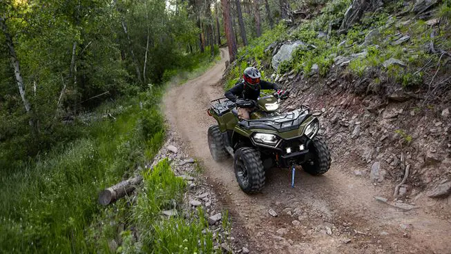 A rider on a Polaris Sportsman 570 ATV driving on a well-ridden trail in the forest.