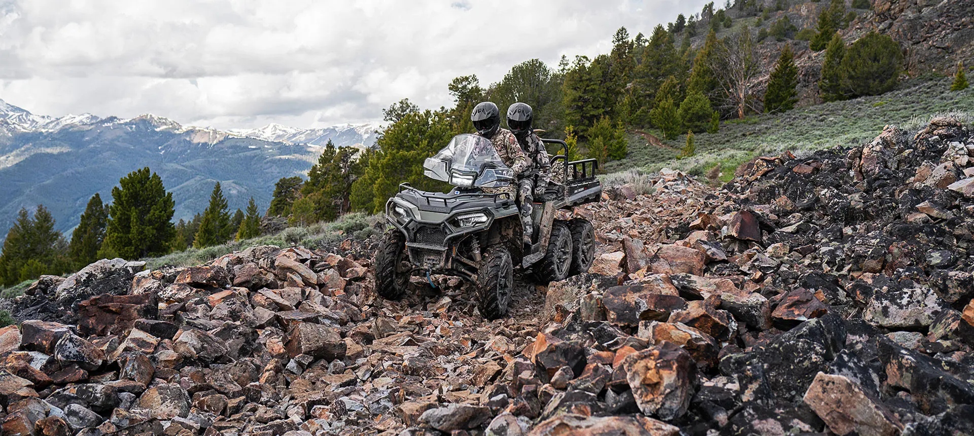 Two hunters riding over rocky terrain on a Polaris Sportsman 6x6 570 ATV.