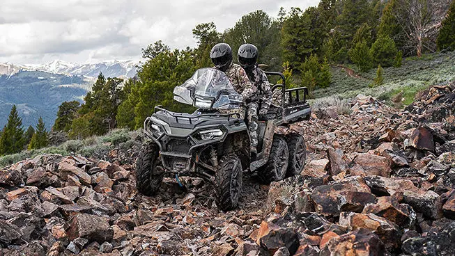 Two hunters riding over rocky terrain on a Polaris Sportsman 6x6 570 ATV.