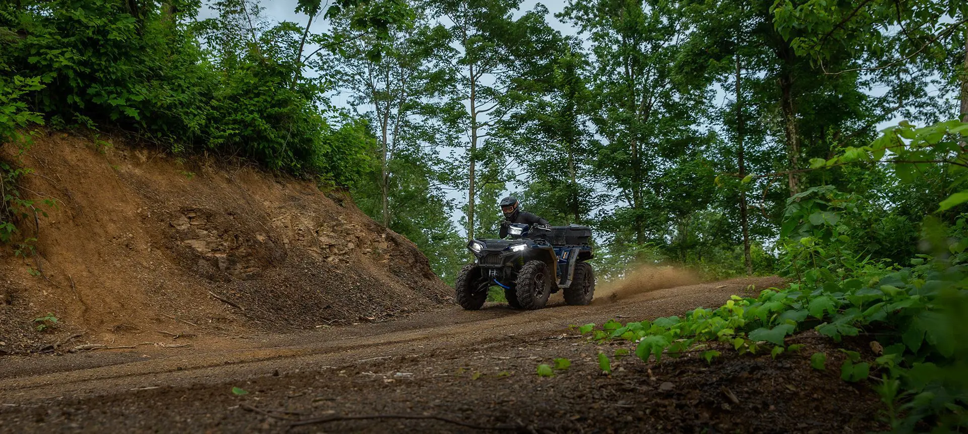 A rider on a Polaris Sportsman 850 ATV driving down a dirt road trail.