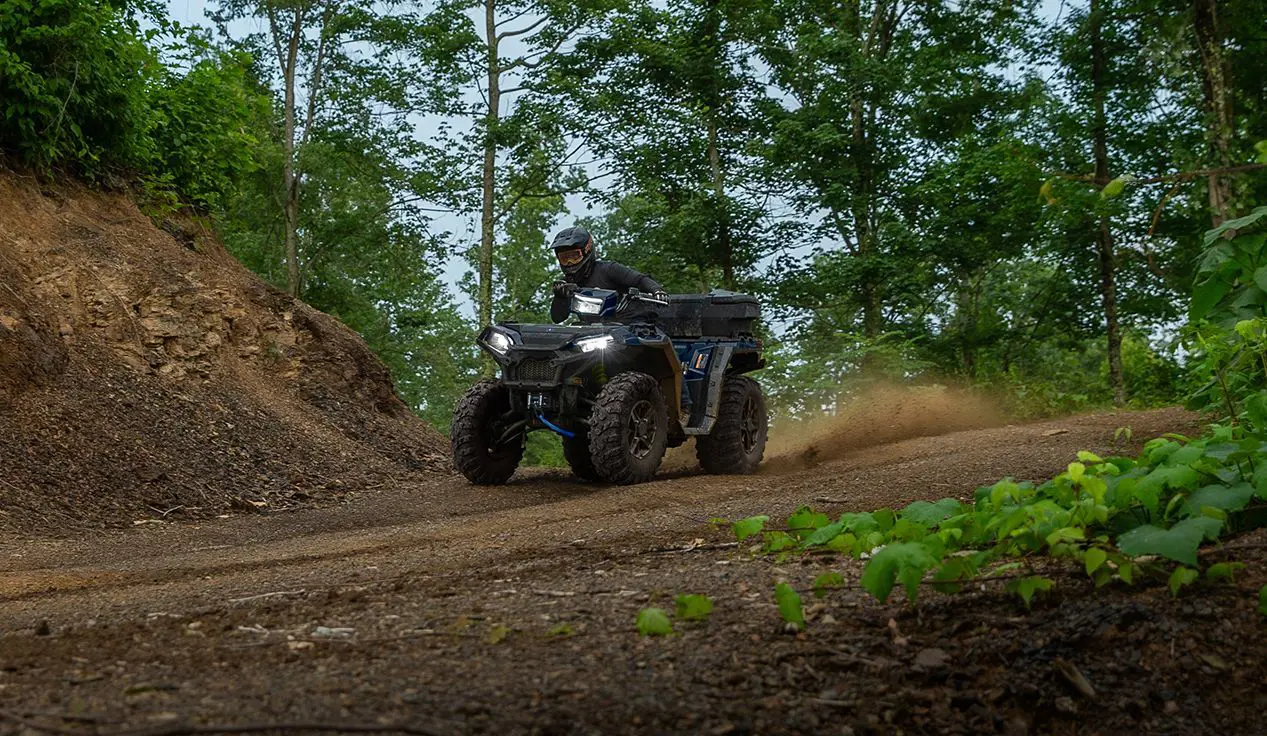A rider on a Polaris Sportsman 850 ATV driving down a dirt road trail.