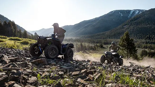 Two Polaris Sportsman 850 ATVs climbing over rocky terrain with ease.