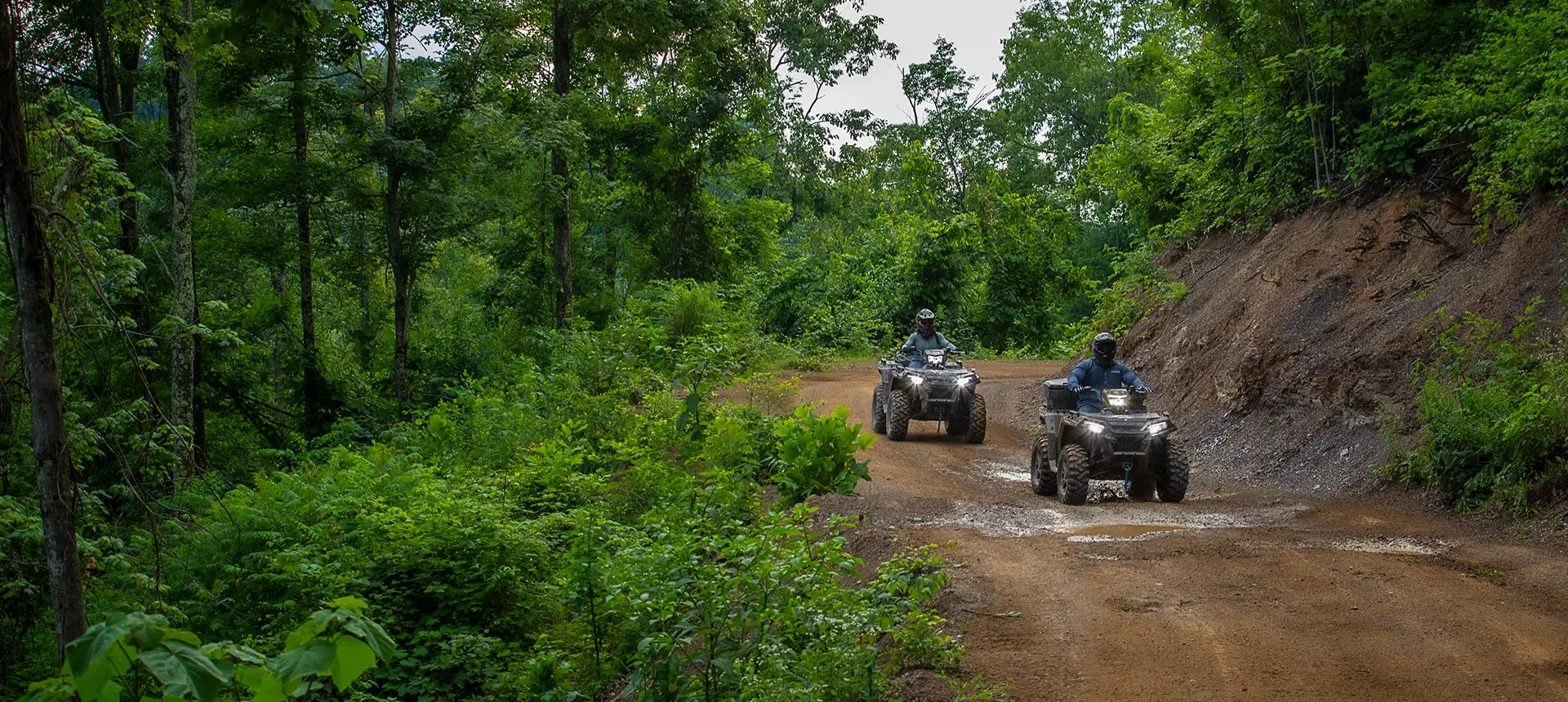 Two Polaris Sportsman 850 ATVs driving on a forest trail.