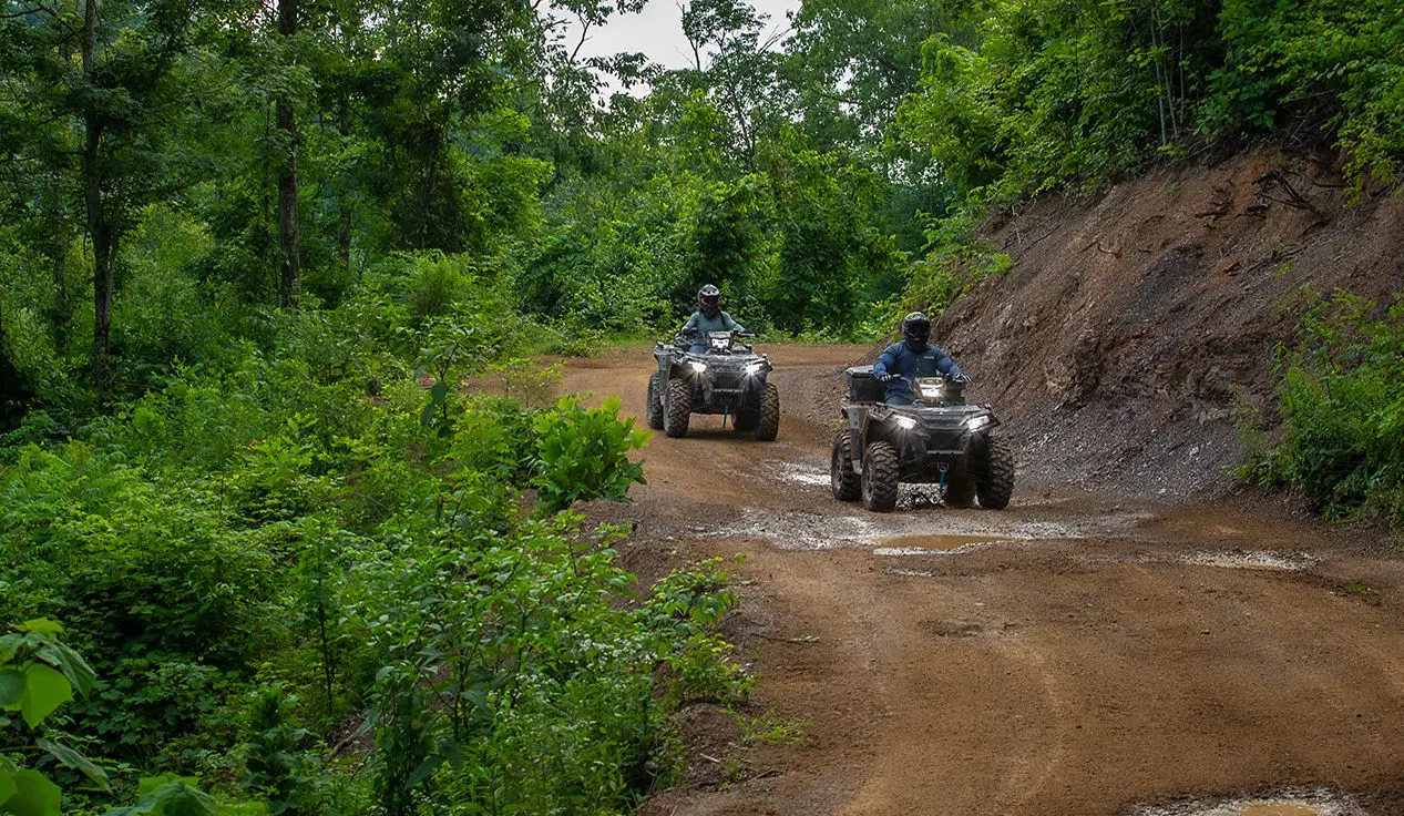 Two Polaris Sportsman 850 ATVs driving on a forest trail.