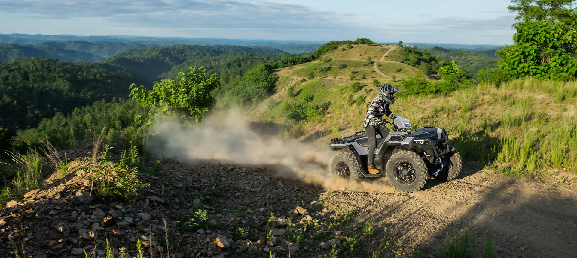 A rider on a  Polaris Sportsman XP 1000 ATV driving on a hilly trail.