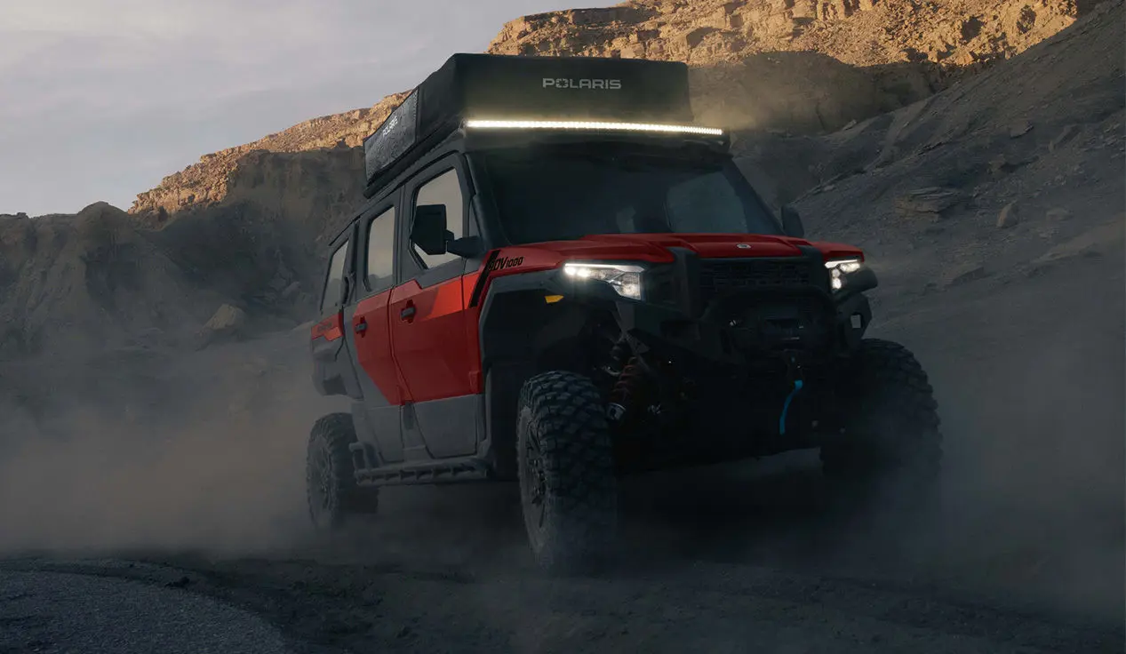 A Polaris XPEDITION ADV 5 NorthStar side-by-side with lights illuminated in the desert.
