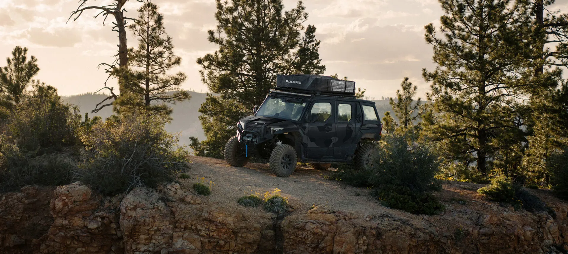 Side profile of a Matte Super Graphite  Polaris XPEDITION ADV 5 NorthStar parked on a hill.
