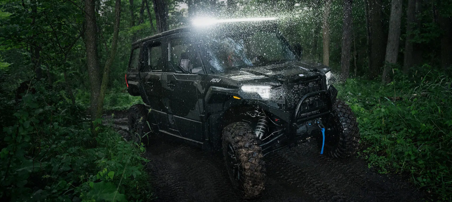A  Polaris XPEDITION ADV 5 NorthStar driving in the forest at night with headlights illuminated.