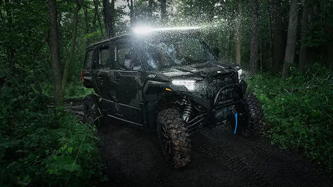 A  Polaris XPEDITION ADV 5 NorthStar driving in the forest at night with headlights illuminated.