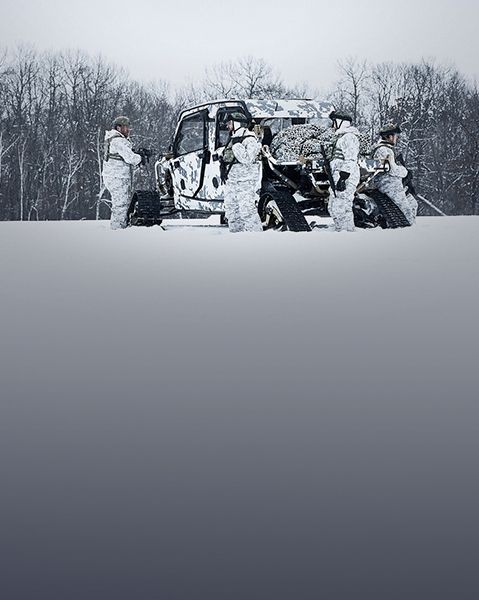 4 soldiers in a snowy field near a Polaris Tactical Vehicle with winter camo.