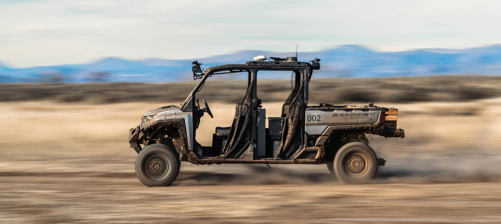 Side profile of a mud-splattered Polaris RANGER CREW XD 1500 speeding across a plain with motion blur.
