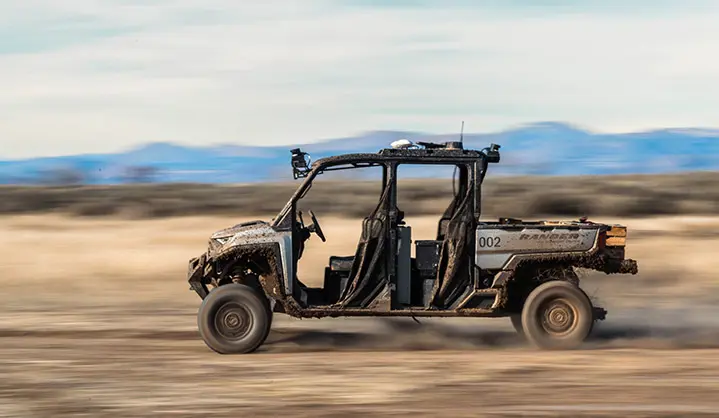 Side profile of a mud-splattered Polaris RANGER CREW XD 1500 speeding across a plain with motion blur.