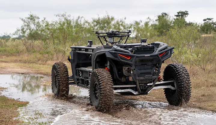 Rear view of a black Polaris RZR XP 1000 equipped with sensors and a drone, splashing through shallow water.