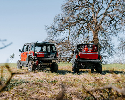 Two Polaris Government and Defense off-road vehicles parked on a grassy field, shown front and rear, with mounted equipment and leafless trees under a clear sky.
