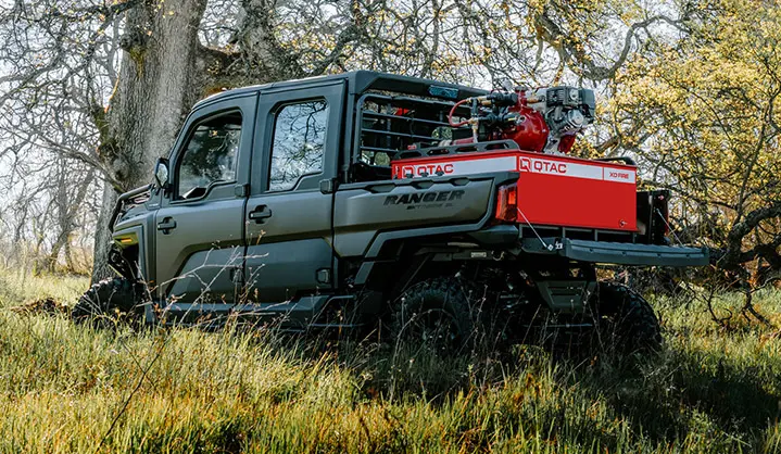 Polaris RANGER CREW XD 1500 NorthStar Edition parked in tall grass with a QTAC firefighting unit mounted in the rear bed, surrounded by trees in a wooded outdoor setting.