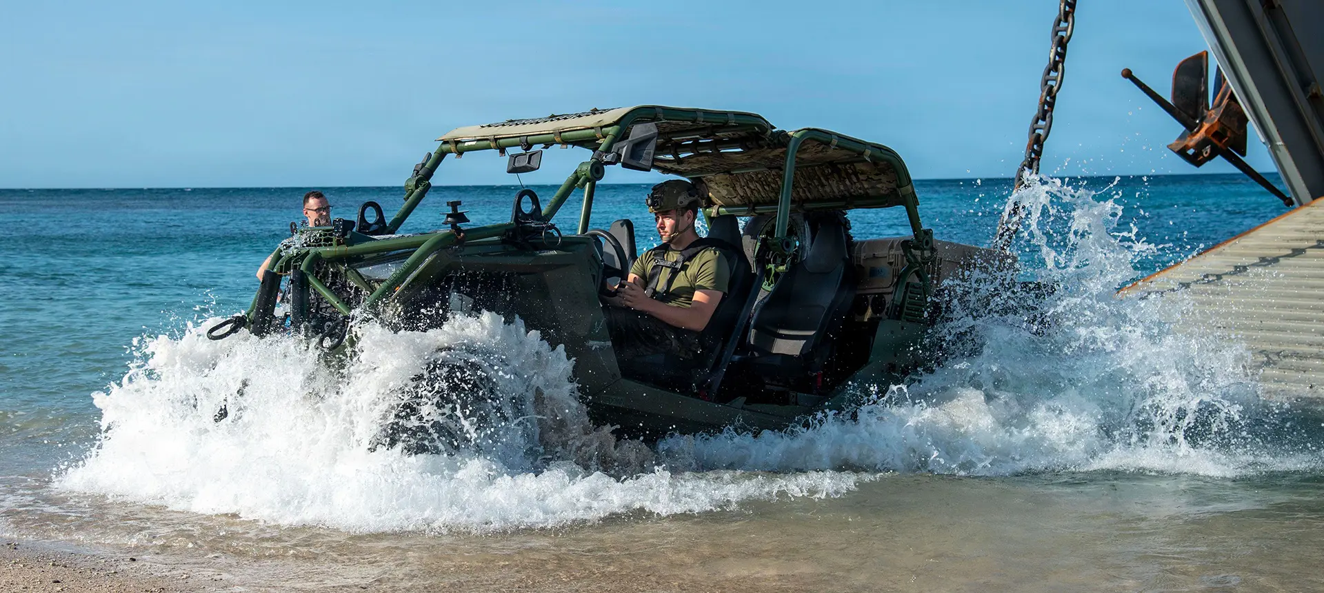 Military personnel loading equipment onto a Polaris MRZR military Side-by-Side vehicle in wet outdoor conditions with tactical gear mounted throughout the vehicle.