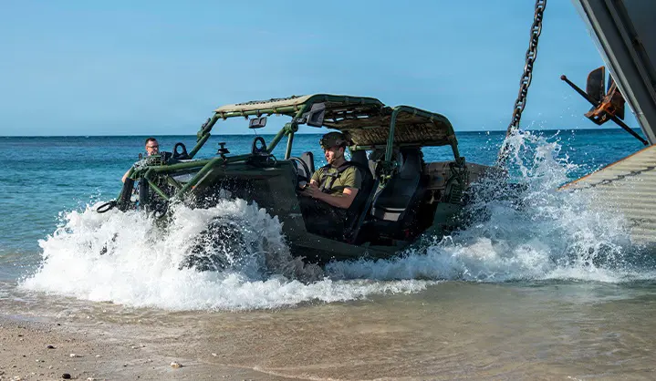 Military personnel loading equipment onto a Polaris MRZR military Side-by-Side vehicle in wet outdoor conditions with tactical gear mounted throughout the vehicle.