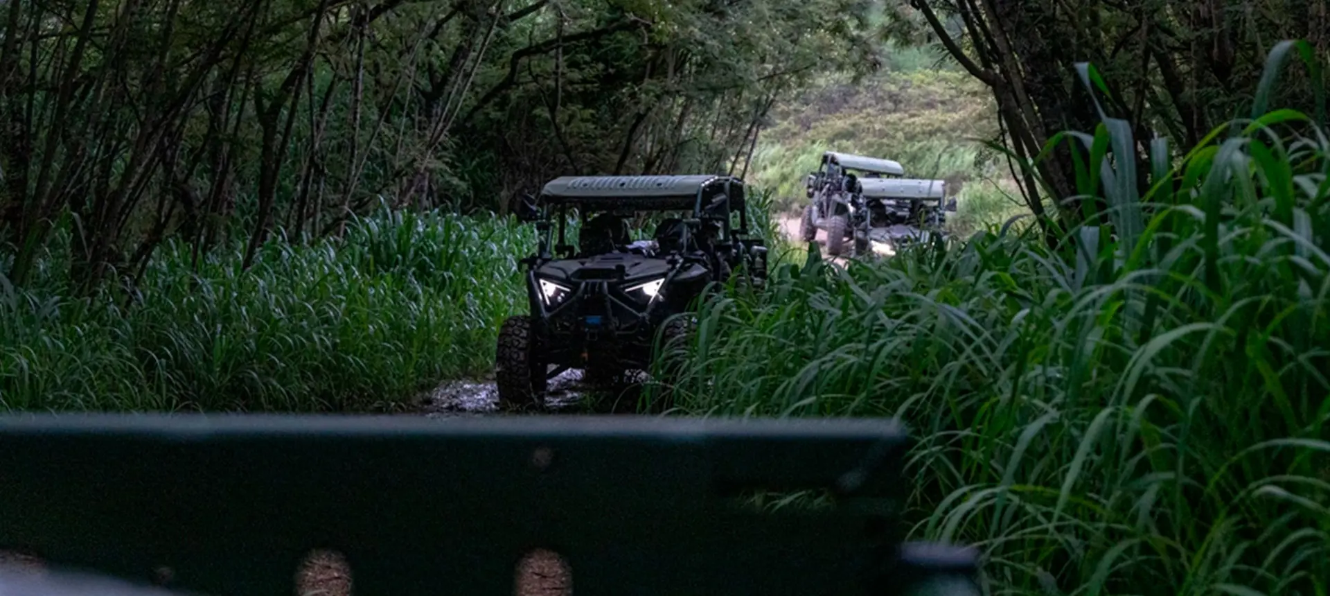 Side profile of a tan Polaris MRZR D4 ultralight tactical vehicle equipped with sensor technology, parked in a forest.