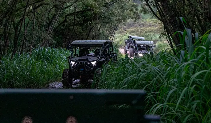 Side profile of a tan Polaris MRZR D4 ultralight tactical vehicle equipped with sensor technology, parked in a forest.