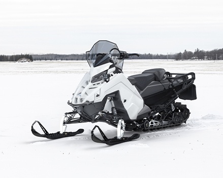 White Polaris Military 850 Voyageur 155 Crossover snowmobile with a windshield, two-up seat and rear cargo rack parked in a snowy field.