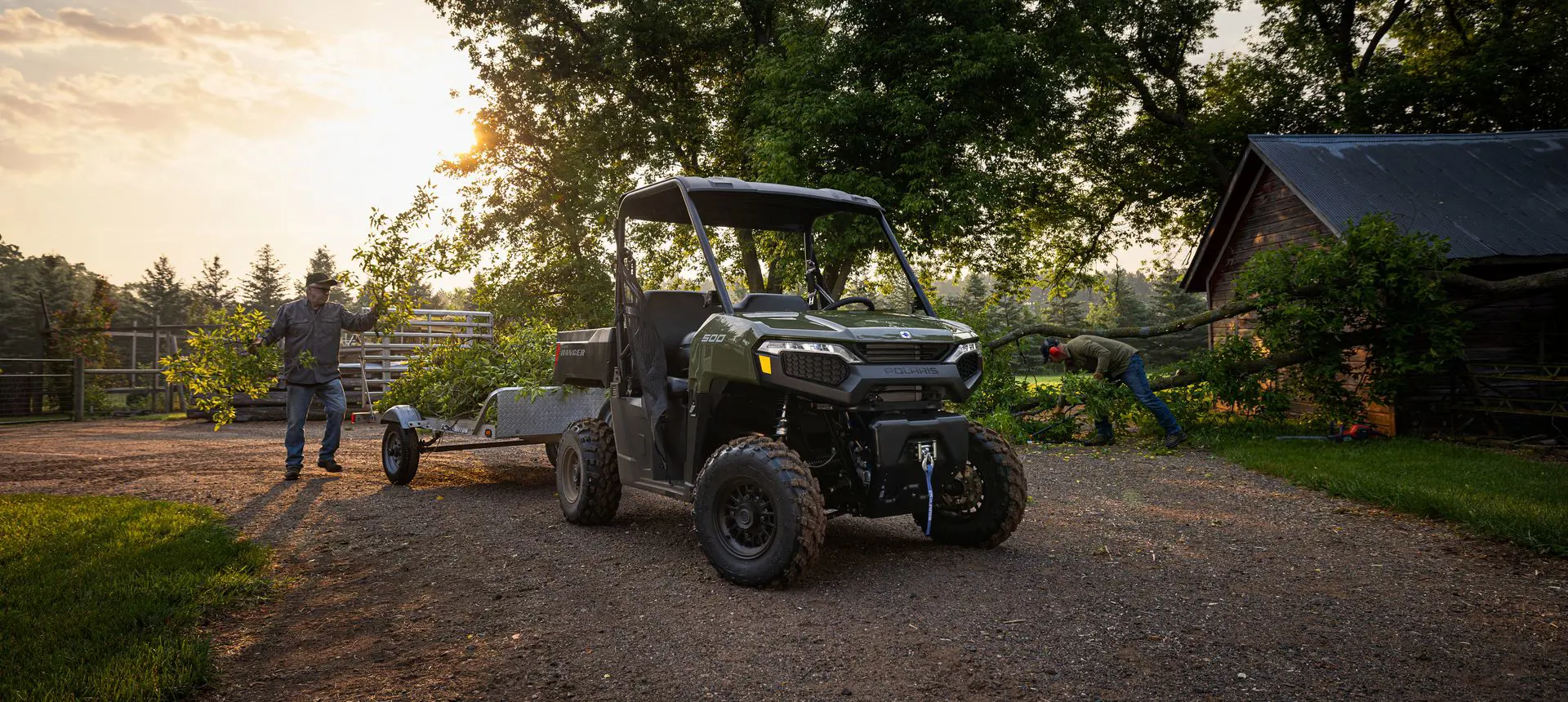 2 men clearing a fallen tree and putting branches into the cargo box of their Polaris RANGER 500 UTV.