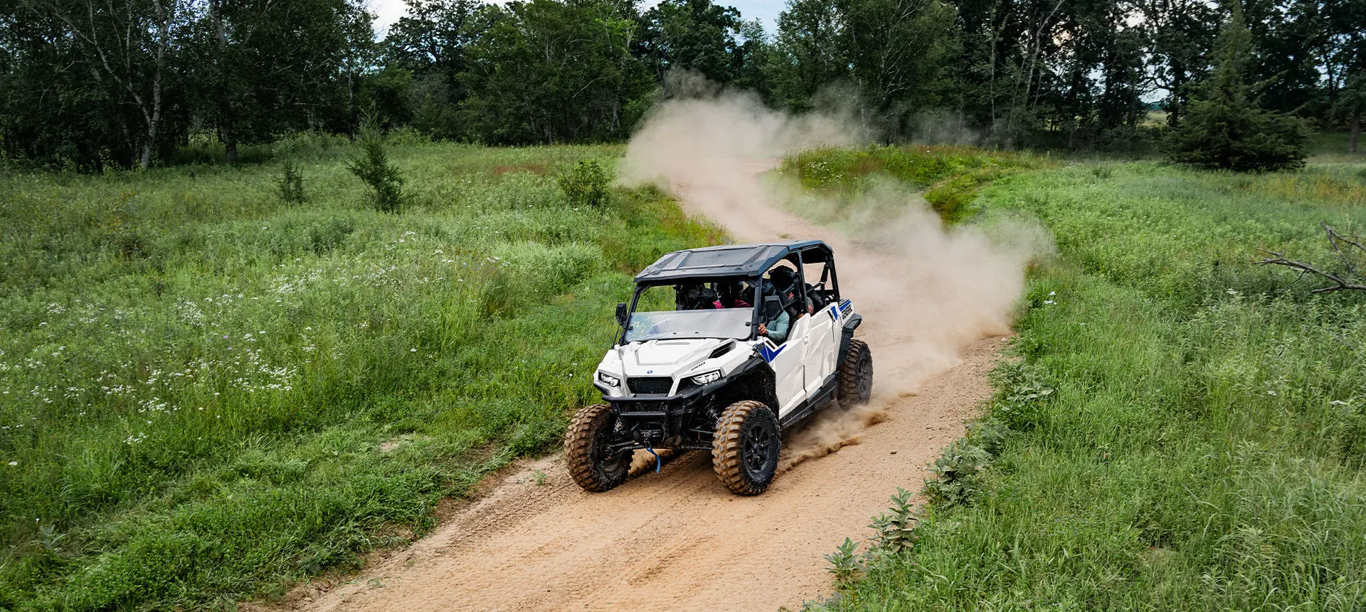 Aerial view of a Polaris GENERAL XP 4 1000 side-by-side driving down a dusty trail with 4 riders.