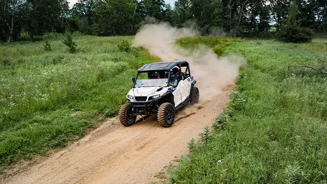 Aerial view of a Polaris GENERAL XP 4 1000 side-by-side driving down a dusty trail with 4 riders.