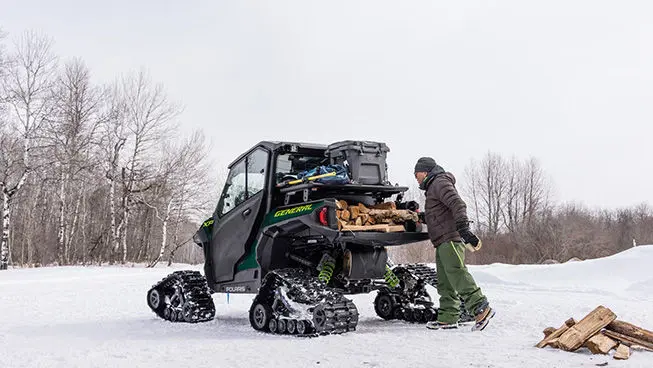 A person loading firewood into the cargo box of a winterized Polaris GENERAL XP 1000 side-by-side in the winter.