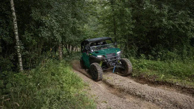 Front end view of a Polaris GENERAL XP 1000 side-by-side with headlights illuminated driving on a forest trail.