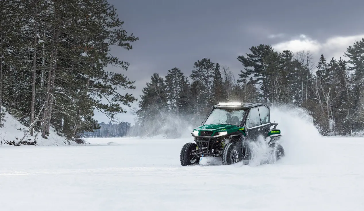 A Polaris GENERAL XP 1000 side-by-side with lightbar and full door accessories installed driving through a snowy field.