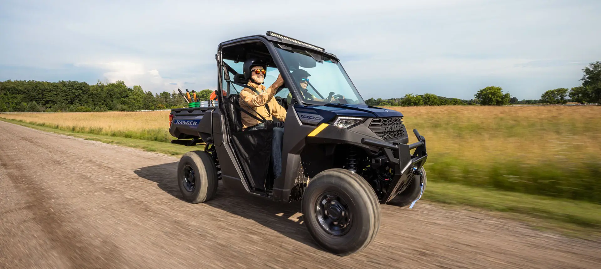 Polaris RANGER 1000 UTV cruising a dirt road with 2 riders inside.