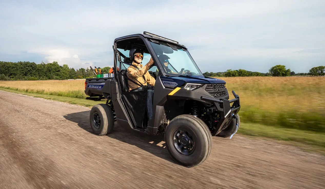 Polaris RANGER 1000 UTV cruising a dirt road with 2 riders inside.