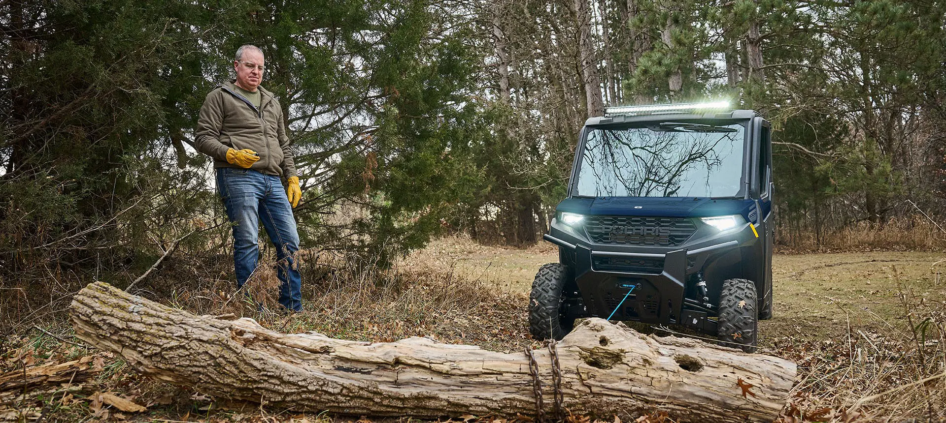 A man using the winch on his Polaris RANGER 1000 CAB UTV to move a log.