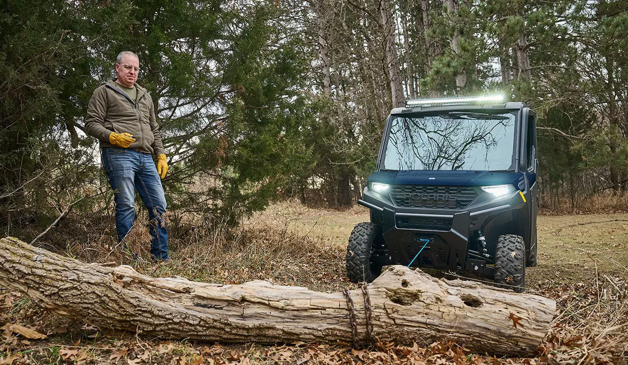 A man using the winch on his Polaris RANGER 1000 CAB UTV to move a log.