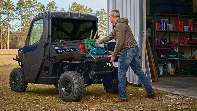 A man loading gear into the cargo box of his Polaris RANGER 1000 CAB enclosed UTV.