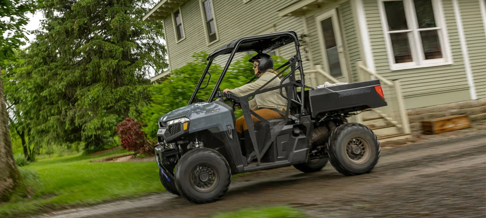 A person driving through their yard in a Polaris RANGER 500 UTV.